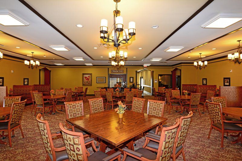 A spacious dining room with multiple tables and chairs, featuring a chandelier.