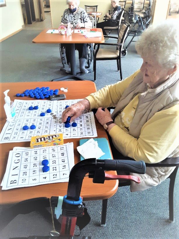 An elderly woman playing bingo at a table indoors.