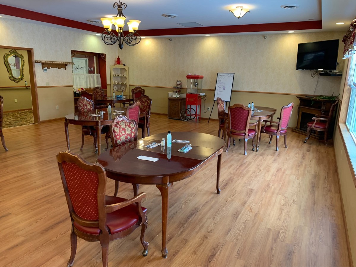 A dining room with elegant chairs, tables, and a chandelier, featuring a wooden floor and a whiteboard.