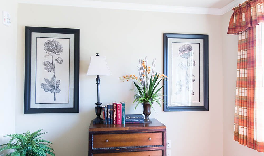 A neatly decorated dresser with books, a lamp, plant, and framed art on the wall.