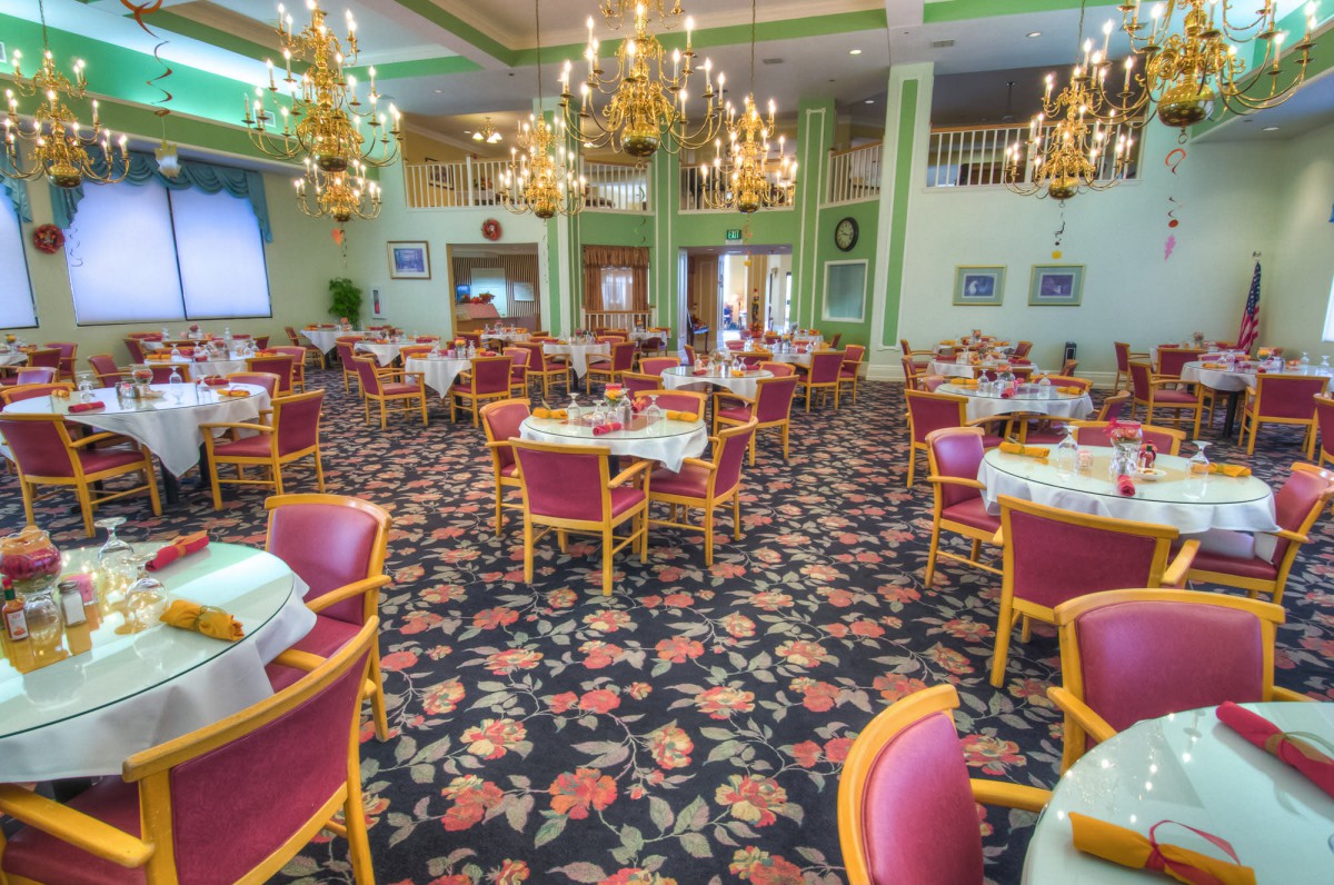 An elegant dining area with floral carpet and chandeliers, featuring neatly arranged tables and chairs.