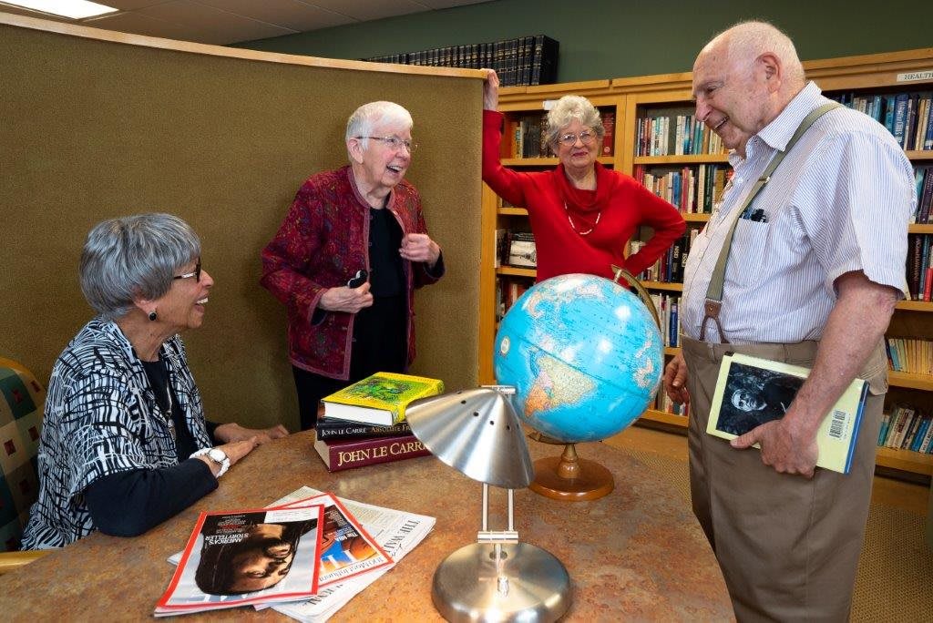 A group of seniors engaging in a discussion surrounded by books and a globe in a library.
