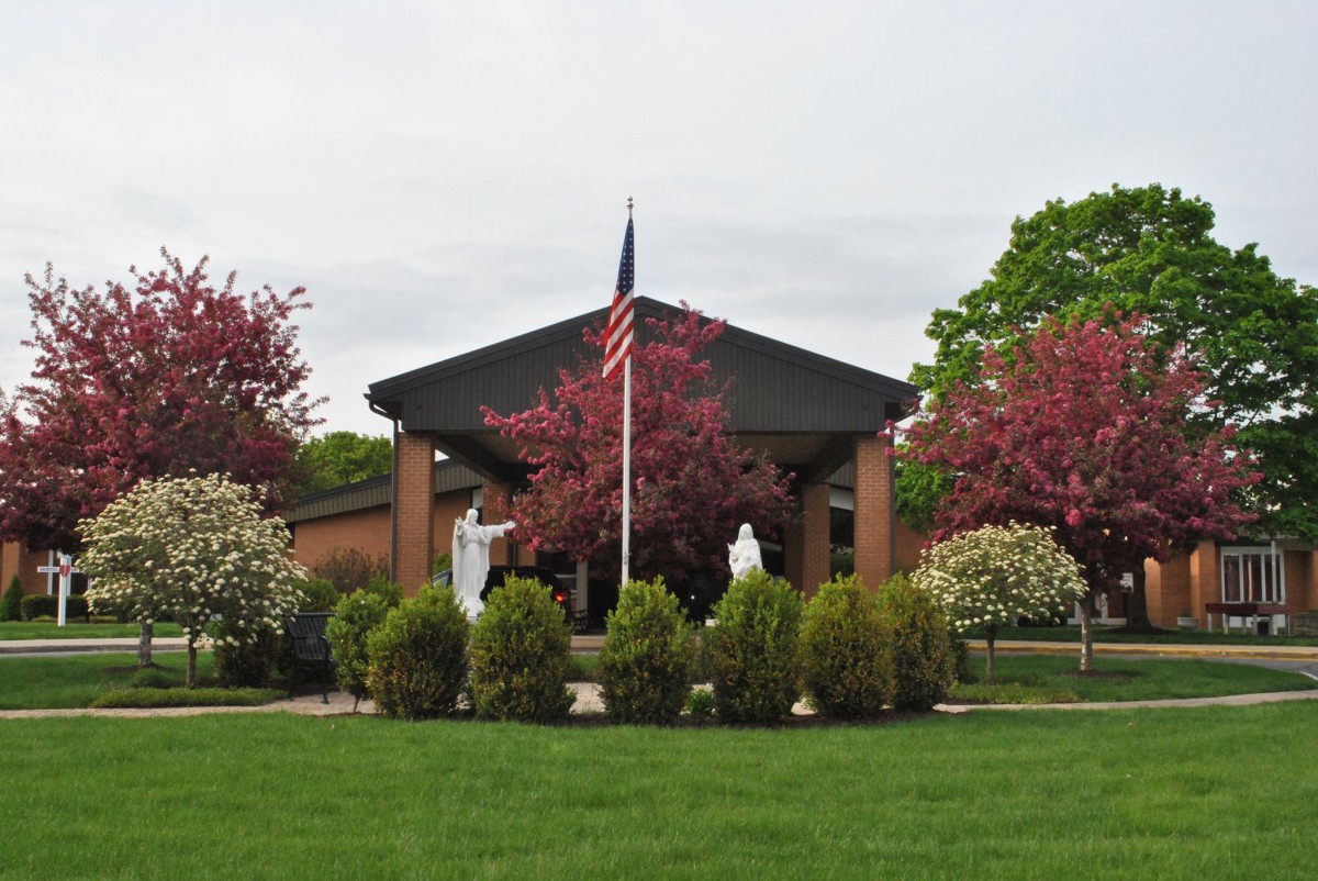 A building with an American flag, surrounded by statues, shrubs, and blossoming trees.