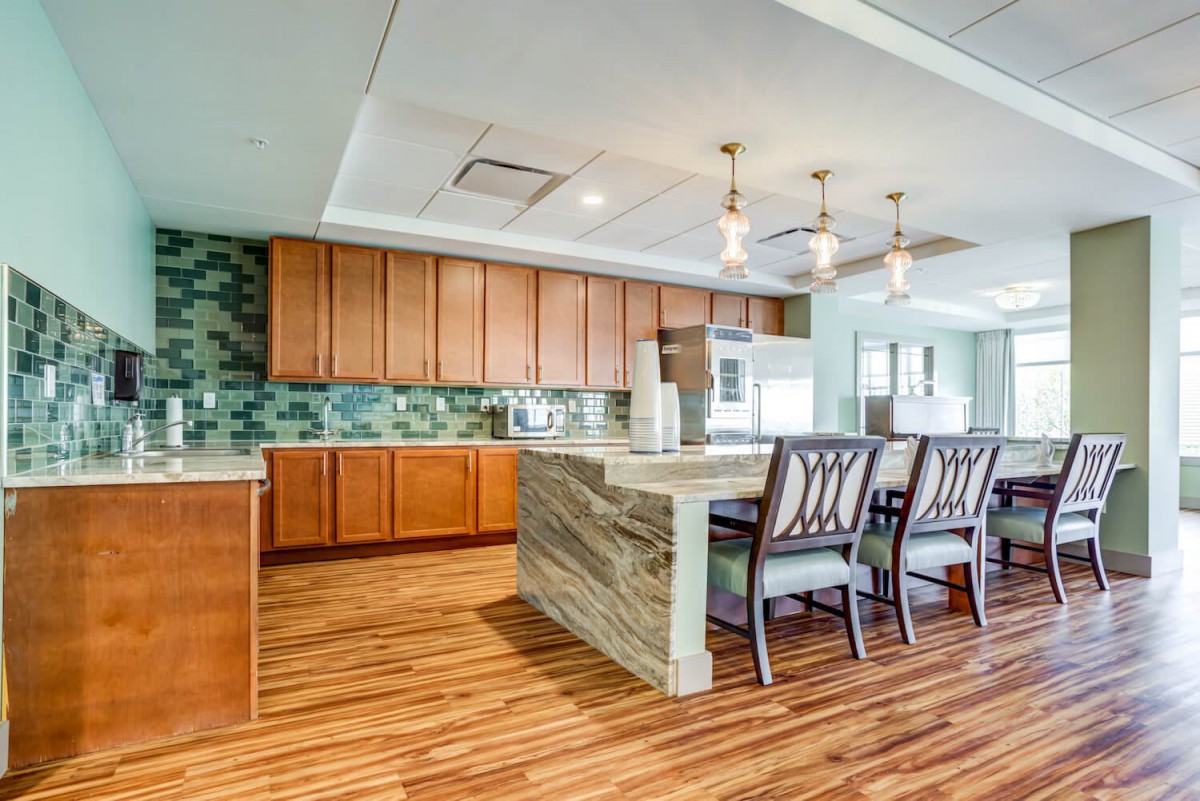 A modern kitchen featuring an island with seating, wooden flooring, and stylish pendant lights.