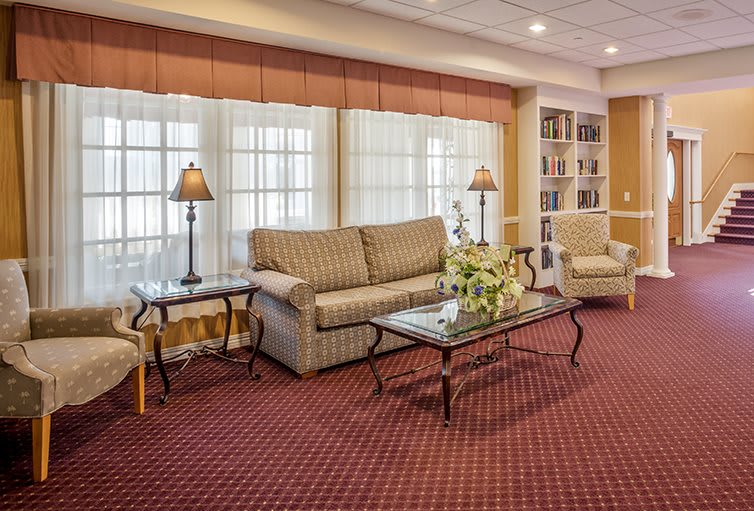 A cozy living room with a sofa, armchairs, and a glass coffee table on a red carpet.