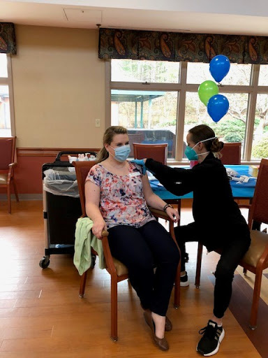 A nurse administers a vaccine to a patient in a healthcare setting, surrounded by decorations.