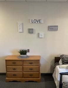 A minimalist bedroom setup with a wooden dresser, decorative plant, and wall art displaying the word 'LOVE' above.