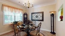 A dining room featuring a round glass table, ornate chairs, a chandelier, and a wall clock.