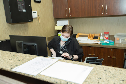 A receptionist in a medical office, wearing a mask while working at a computer.