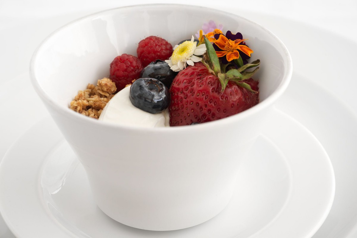 A bowl of yogurt topped with fresh berries, granola, and edible flowers.