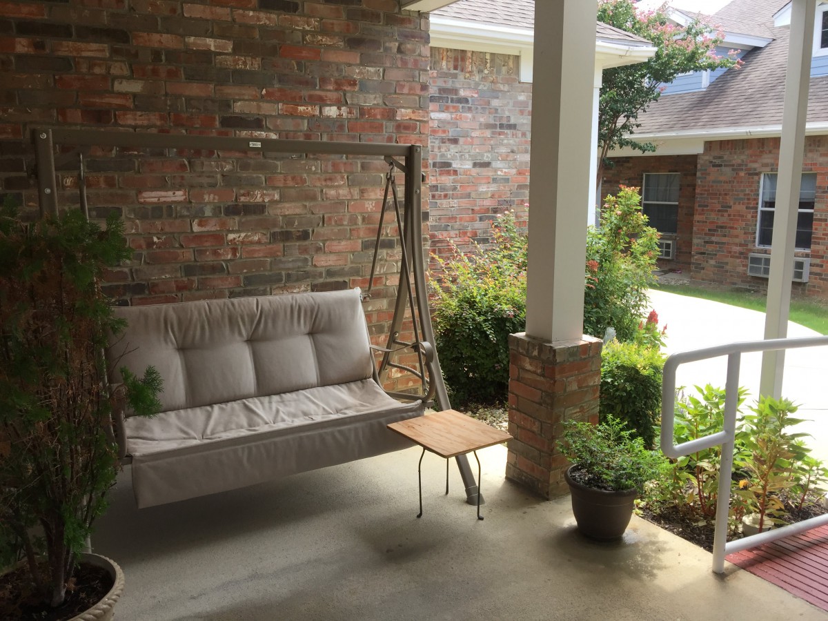 A cozy porch with a swing, small table, and potted plants.