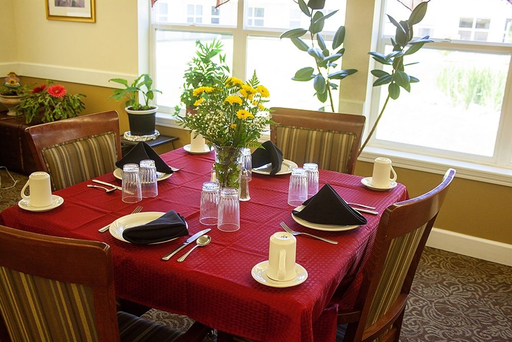 A dining table set for six with a red tablecloth, black napkins, and a floral centerpiece.