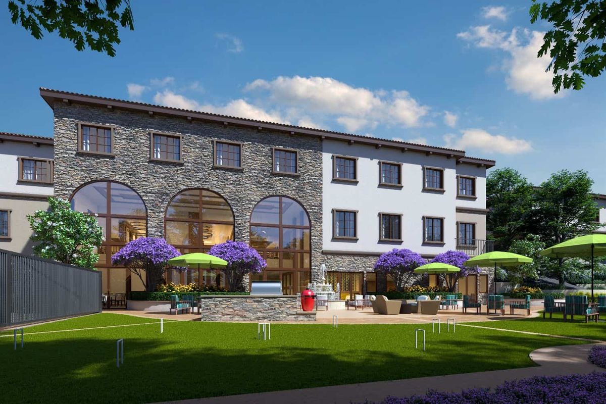 A charming building with a stone facade and outdoor seating area, adorned with purple flowers and green umbrellas under a clear blue sky.