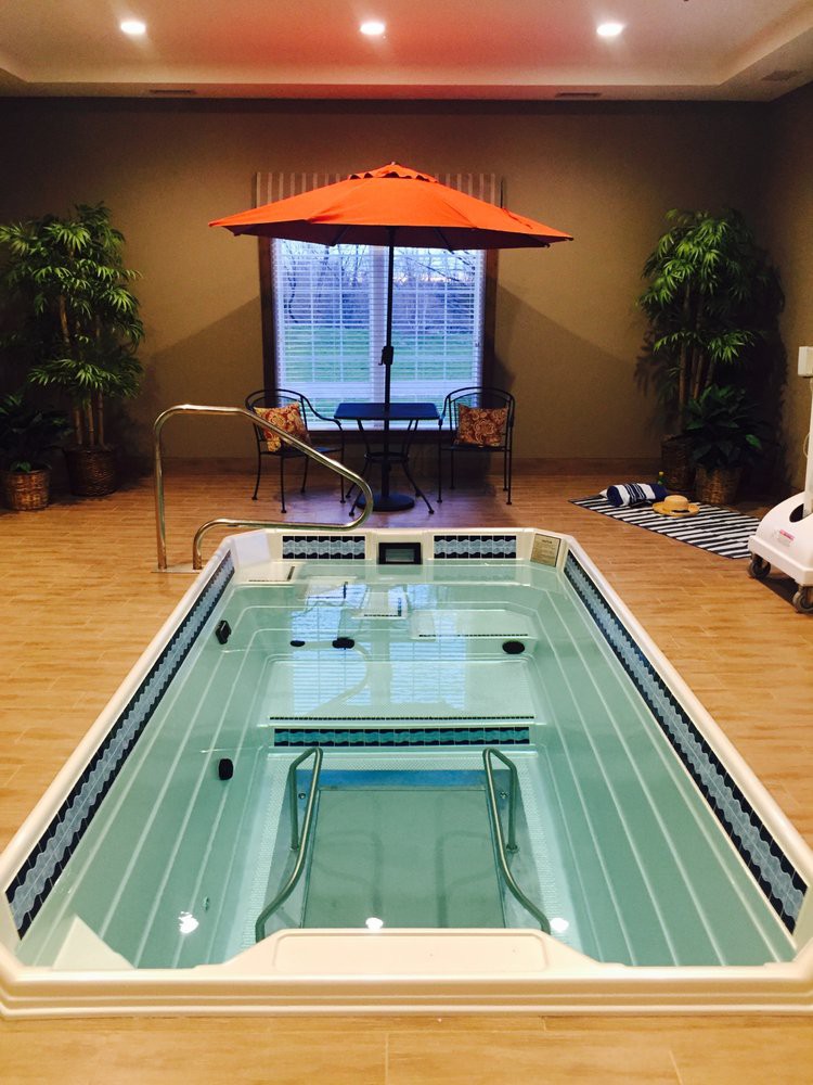 A luxurious indoor swimming pool with an umbrella and surrounding plants, creating a serene relaxation space.