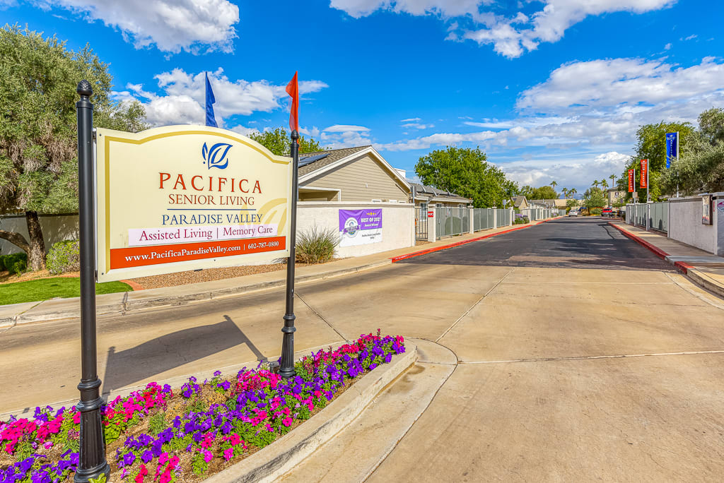 Entrance sign to Pacifica Senior Living facility with colorful flowers and a clear blue sky.