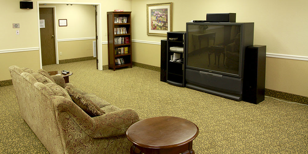 A cozy living room with a large television, bookshelf, and comfortable seating.