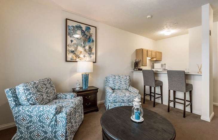 A cozy living space featuring two patterned armchairs, a coffee table, and a kitchen counter with bar stools.