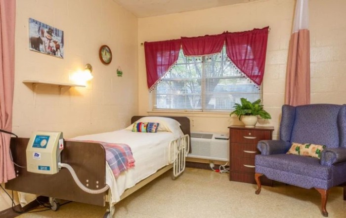 A cozy bedroom with a single bed, decorated with bright curtains and a plant on the dresser.