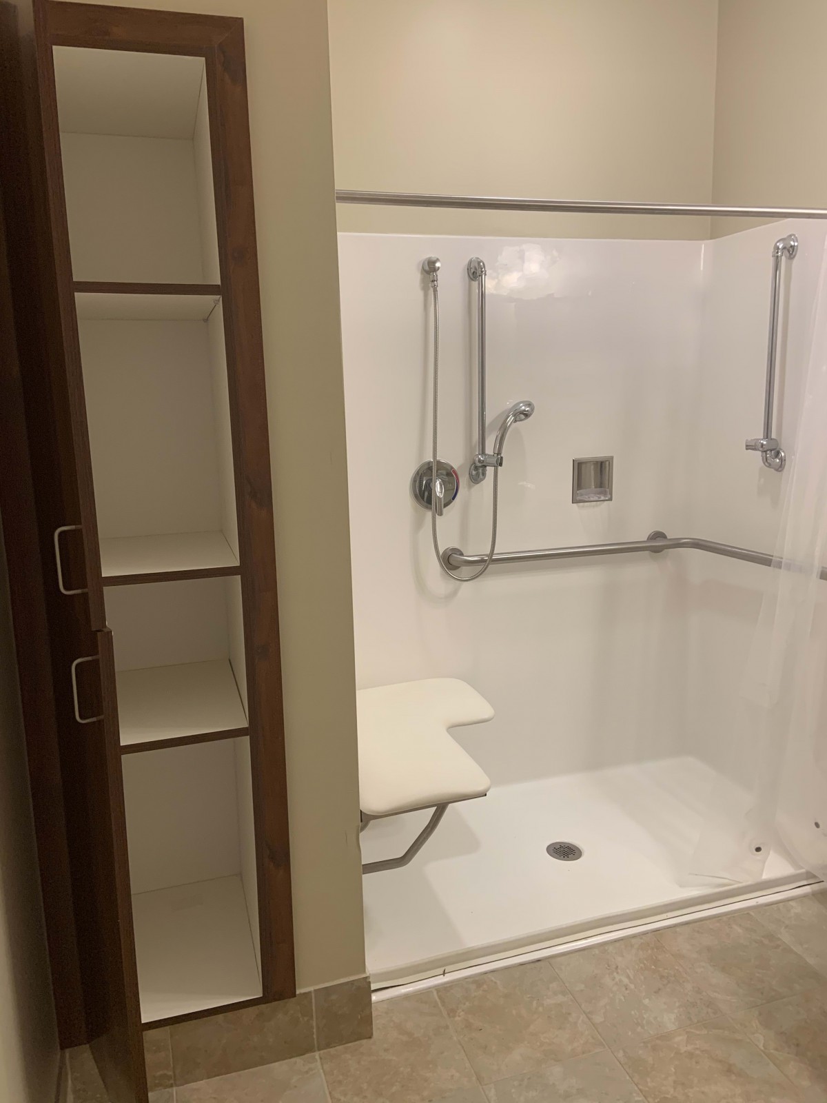 An accessible bathroom with a shower featuring grab bars and a built-in shower chair, alongside shelving.