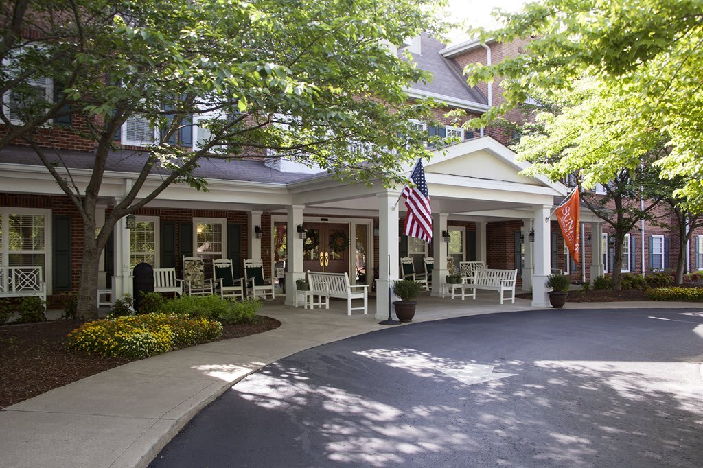 A welcoming entrance to a building with a spacious porch, surrounded by trees and landscaped greenery.