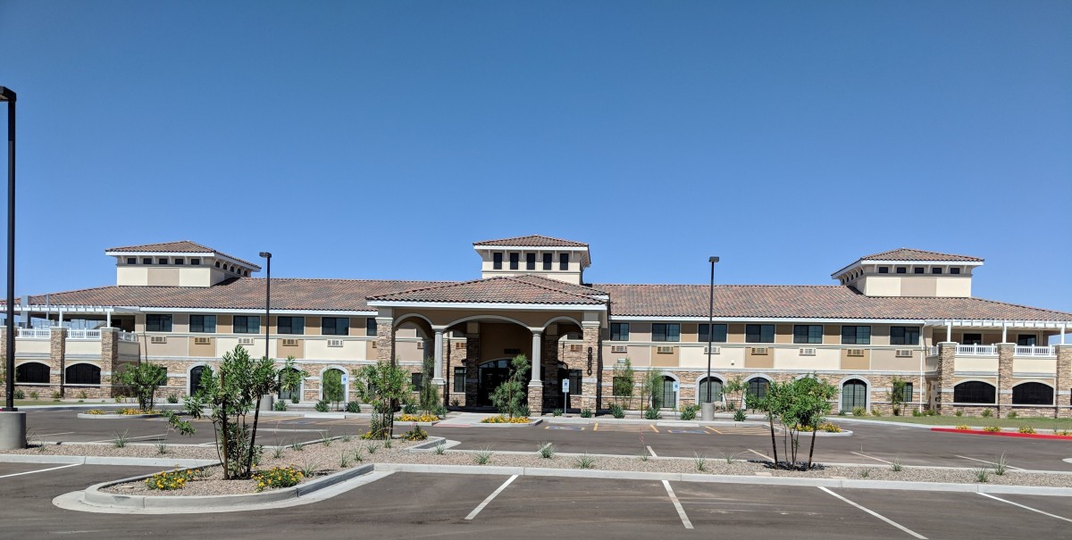 A modern building with an arched entrance and a surrounding parking lot under a clear blue sky.