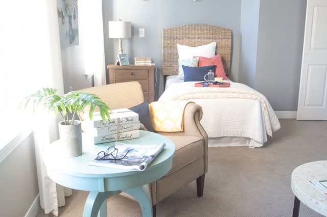 A cozy bedroom with a single bed, an armchair, and a small side table adorned with books and a plant.