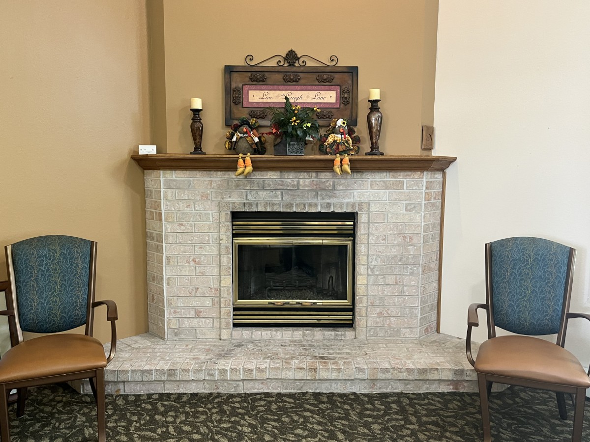 A cozy room with a brick fireplace, decorated mantel, and two chairs.