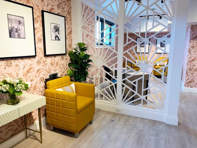 A stylish interior featuring a yellow armchair, framed wall art, plants, and a decorative partition on a wooden floor.