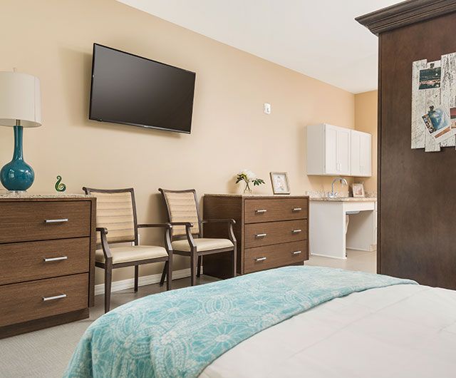 A modern and cozy bedroom featuring a wall-mounted TV, two chairs, and a dresser with decor elements.