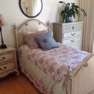 A cozy bedroom with vintage-style decor, featuring a single bed, mirror, and dresser.