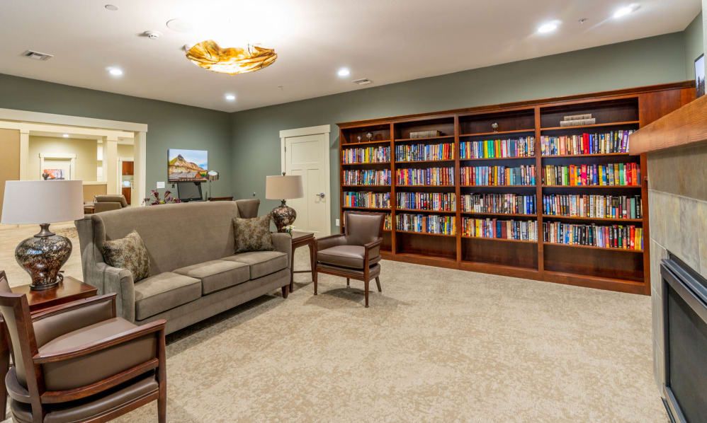 A cozy library room featuring a sofa, armchairs, and extensive bookshelves filled with books.