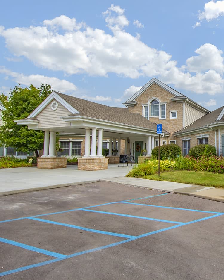 A residential building with a driveway and parking lot under a partly cloudy sky.