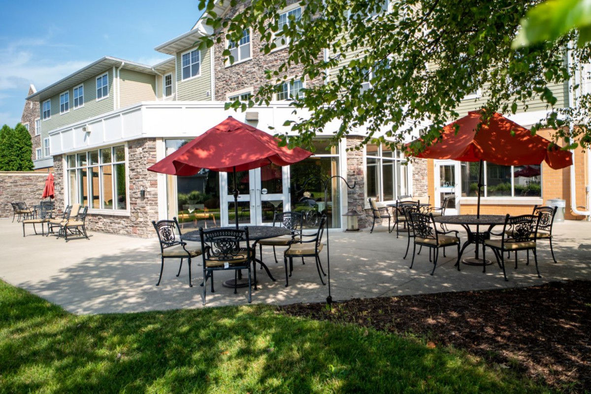 A sunny outdoor patio area with tables and red umbrellas in front of a building.