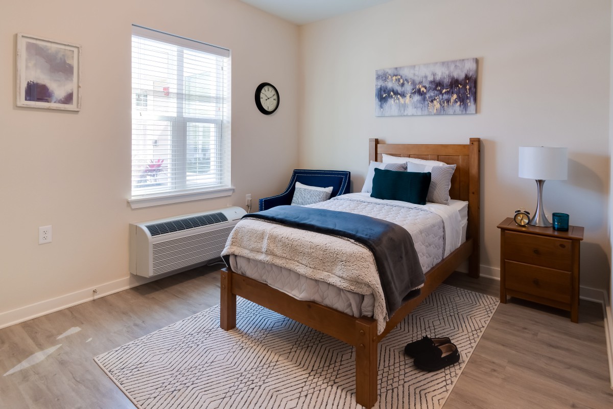 A cozy minimalist bedroom with a single bed, armchair, and natural light from the window.