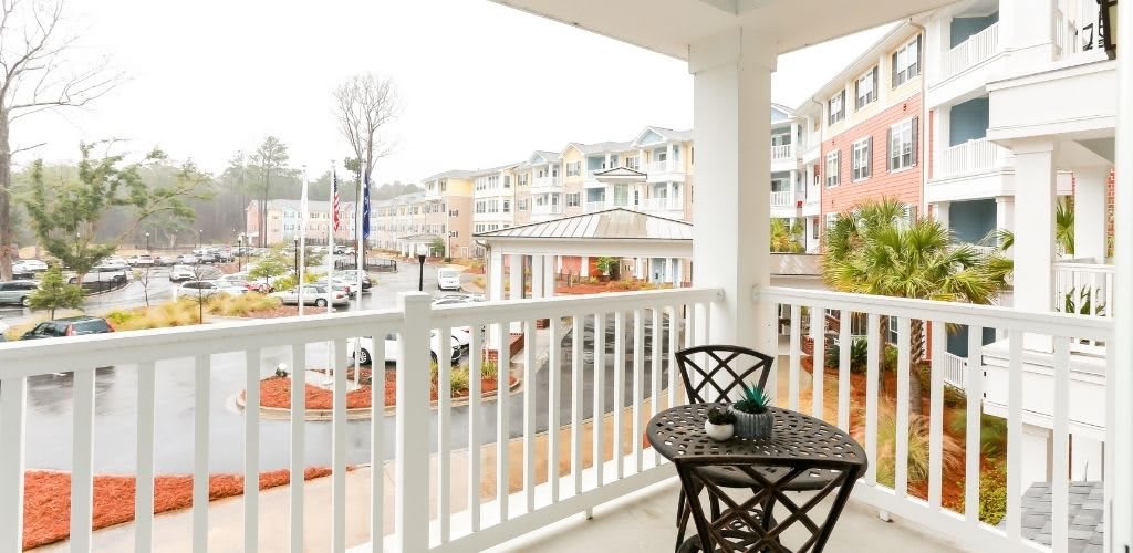 A cozy balcony with a small table and two chairs overlooking a residential area on an overcast day.