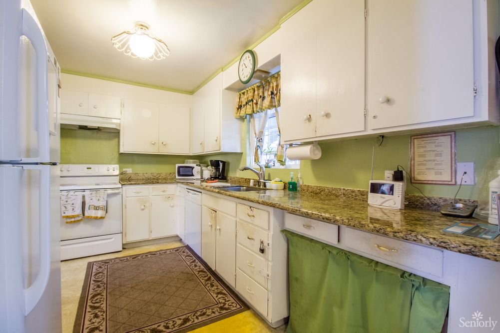 A cozy kitchen with white cabinets and green walls, featuring a granite countertop and retro-style decor.