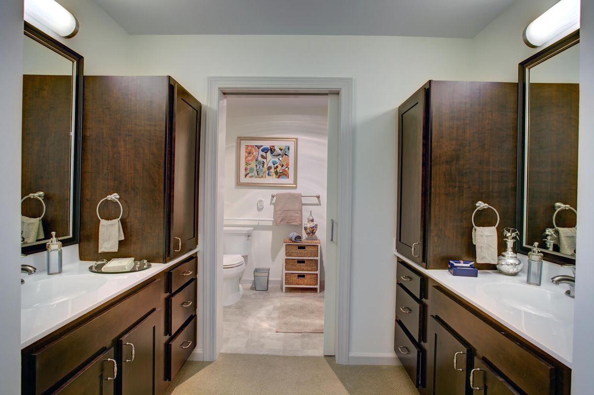 A well-organized bathroom featuring dual sinks with dark wood cabinets and a view into an adjacent room.