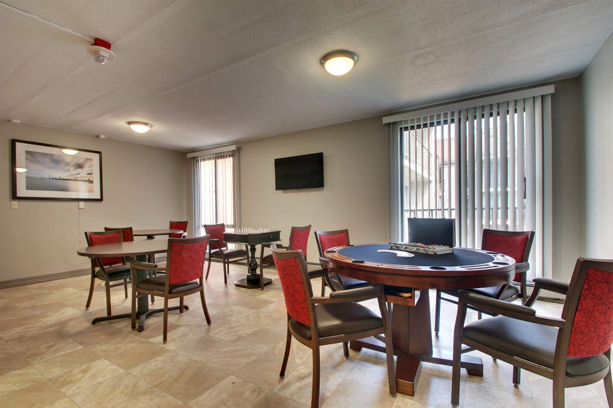 A dining area with several tables and chairs, featuring large windows with blinds.