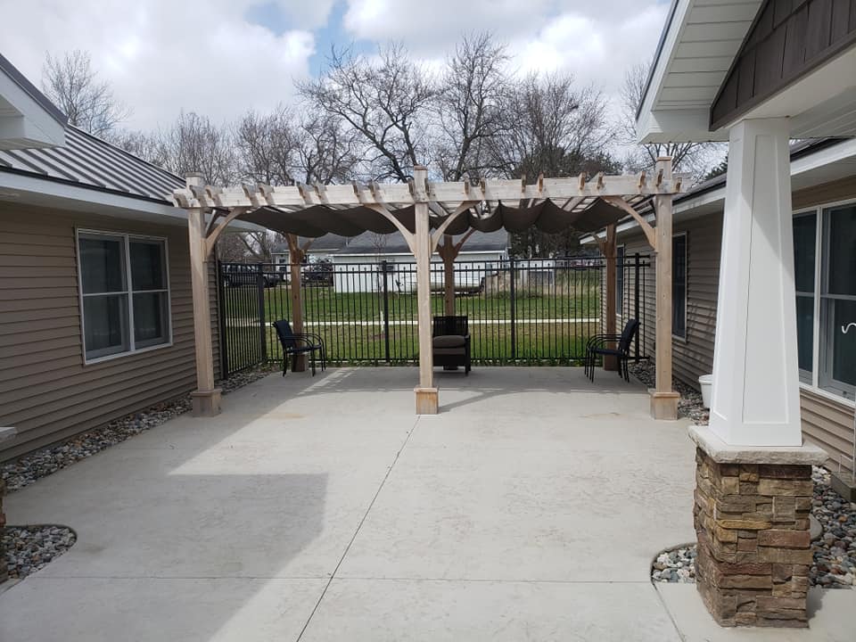 A spacious patio featuring a wooden pergola and outdoor seating, set in a backyard.