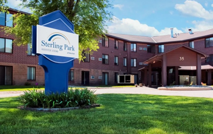 A sunny view of a residential building with a sign in front, surrounded by greenery.
