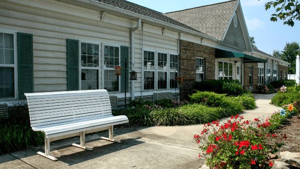 A charming building with a white bench, surrounded by flowers and greenery.