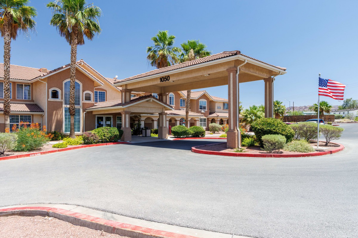 A hotel entrance featuring palm trees and a covered driveway under a clear blue sky.