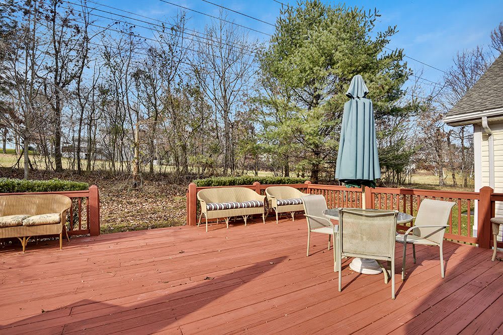 A spacious outdoor deck with patio furniture and an umbrella, surrounded by trees.