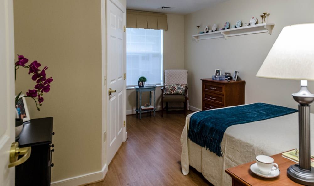 A cozy bedroom with a bed, dresser, and chair situated near a window.