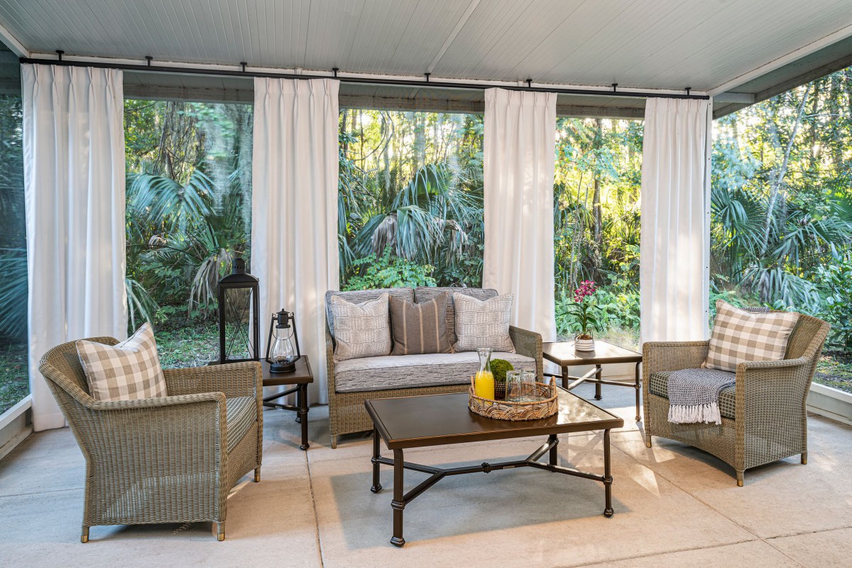 A cozy patio area with comfortable seating, surrounded by lush greenery and natural light.