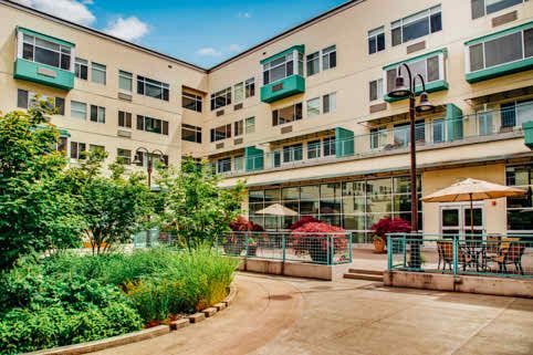 A modern apartment building with a well-maintained courtyard featuring lush vegetation and outdoor seating.