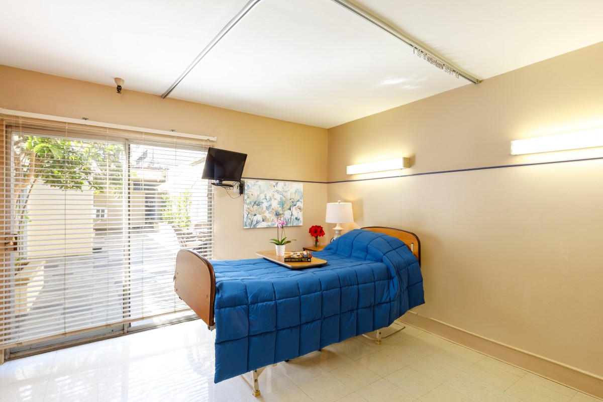 A clean and bright hospital room with a bed, TV, and natural lighting.