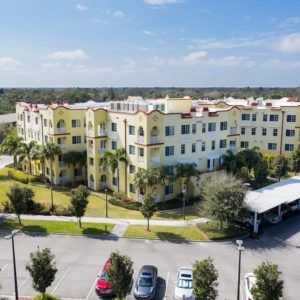 Aerial view of a residential building surrounded by palm trees on a sunny day.