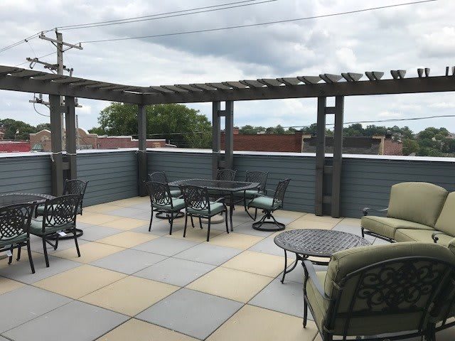 A spacious rooftop patio with comfortable seating under a pergola and a cloudy sky backdrop.