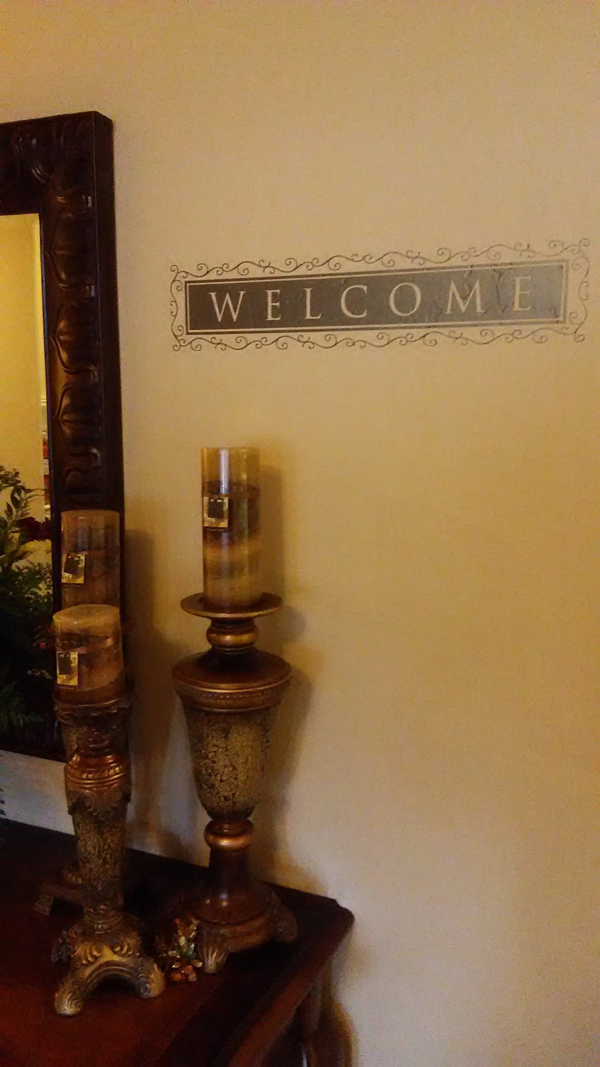 A warmly decorated entryway featuring a welcome sign, ornate candles, and a large mirror.